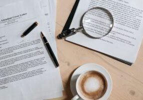 Legal documents with a pen, magnifying glass, and cup of coffee on a wooden desk, symbolizing law research, legal work, and attorney office environment. © Marathon Law Group