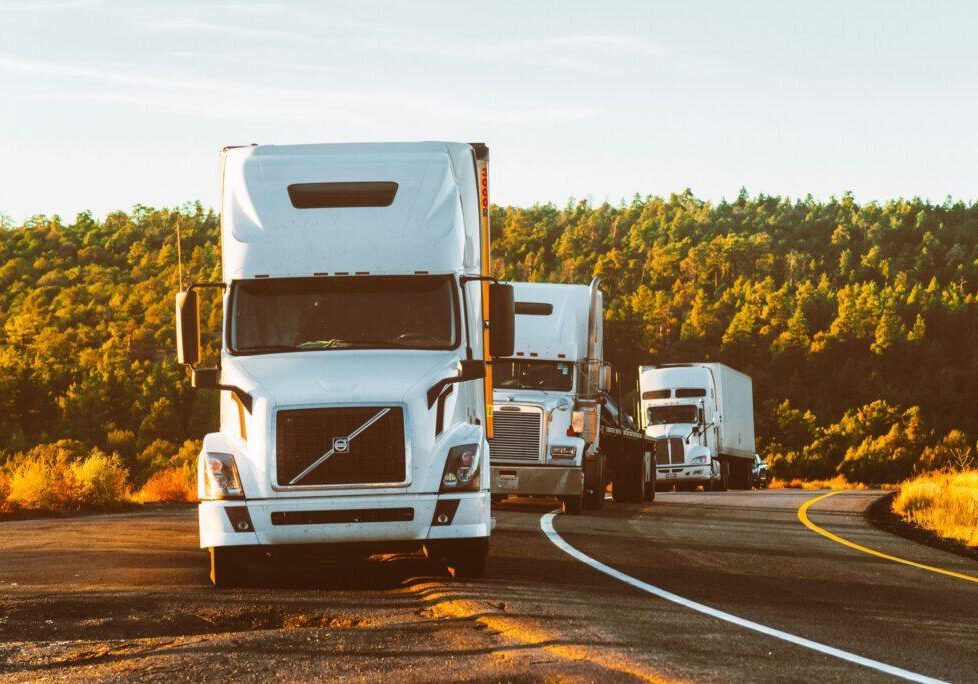 Several white semi trucks driving on a highway with scenic background, representing transportation law, commercial trucking regulations, logistics legal services, and road safety compliance in the legal industry. © Marathon Law Group